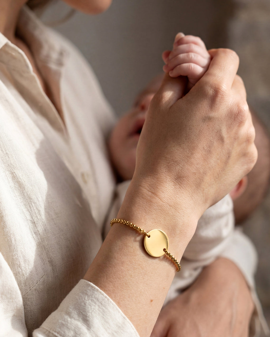 Person holding a baby's hand with a gold bracelet featuring a heart charm.