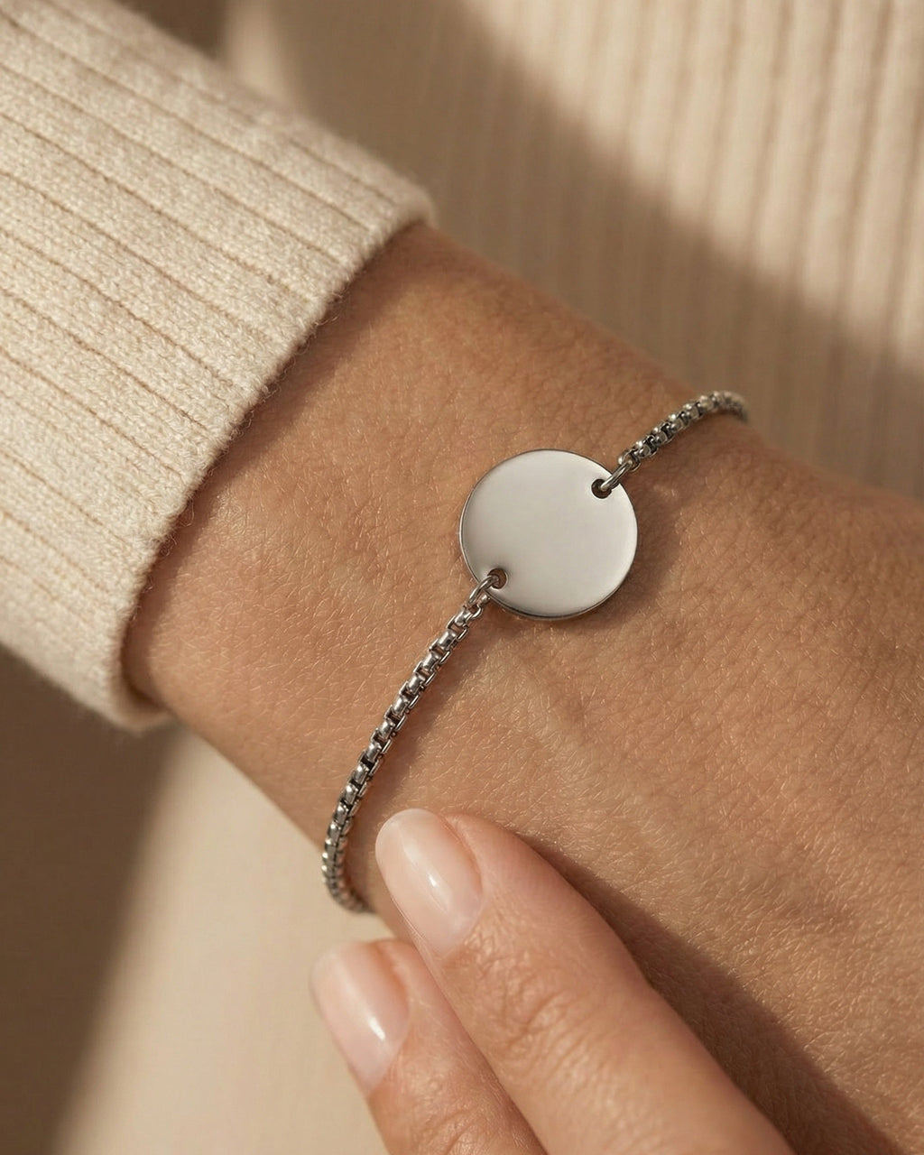 Silver bracelet with a round pendant on a wrist against a beige background