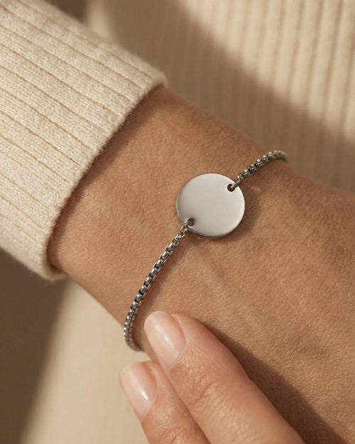 Silver bracelet with a round pendant on a wrist against a beige background