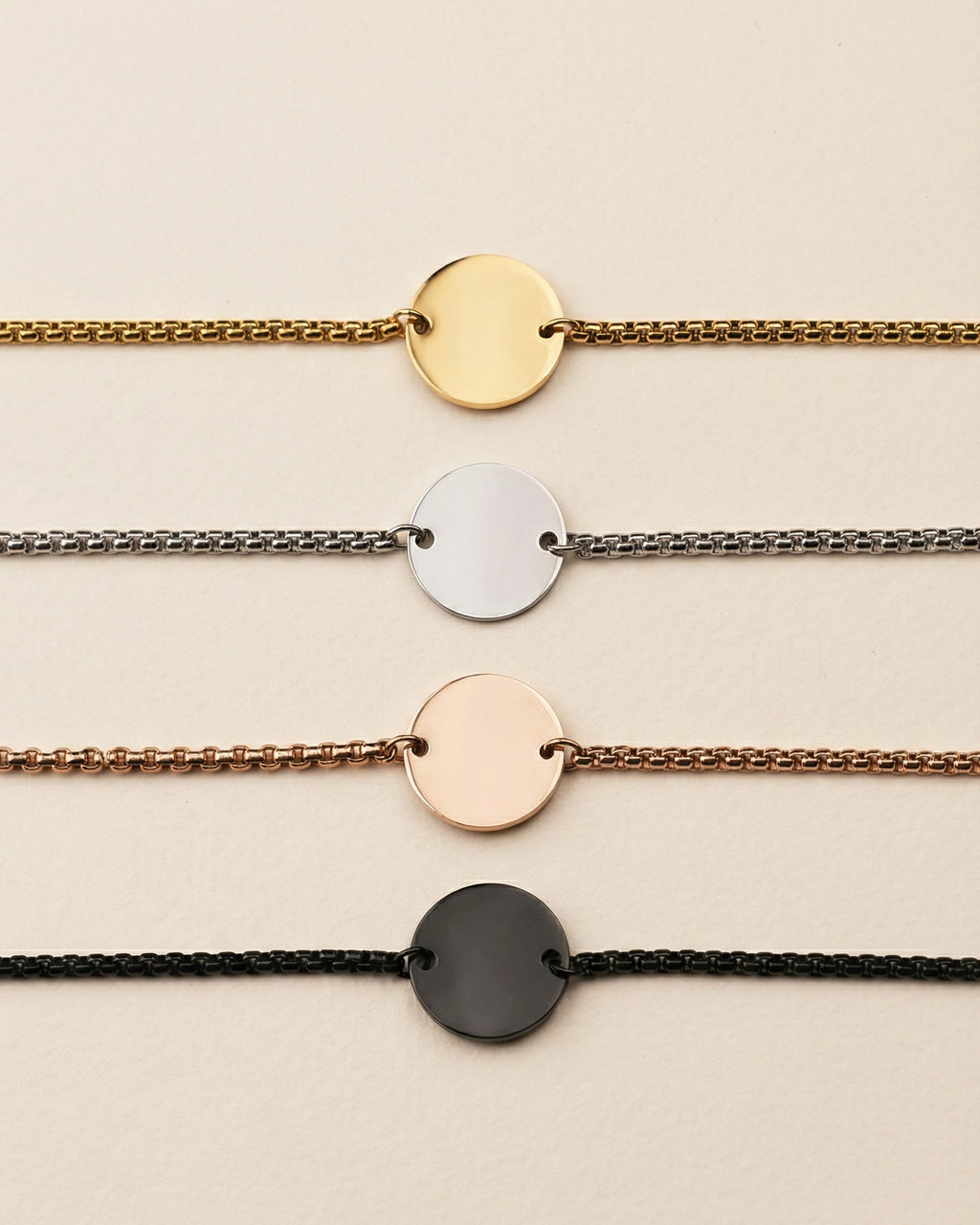 Set of four bracelets with round metal ends on different colored chains against a beige background