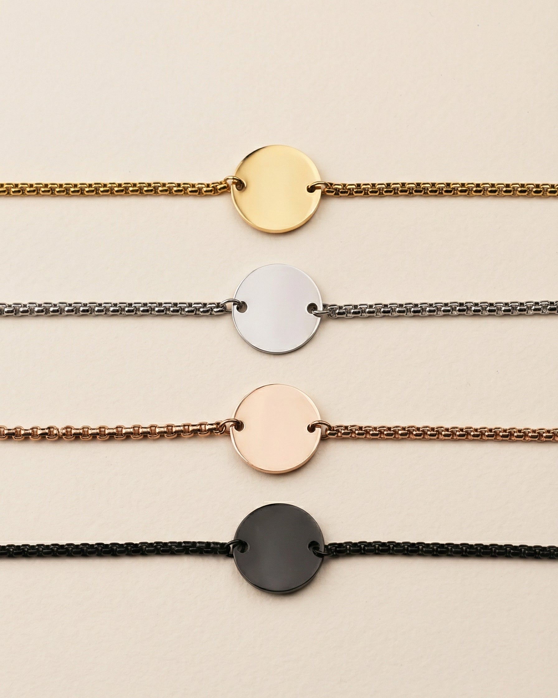 Set of four bracelets with round metal ends on different colored chains against a beige background