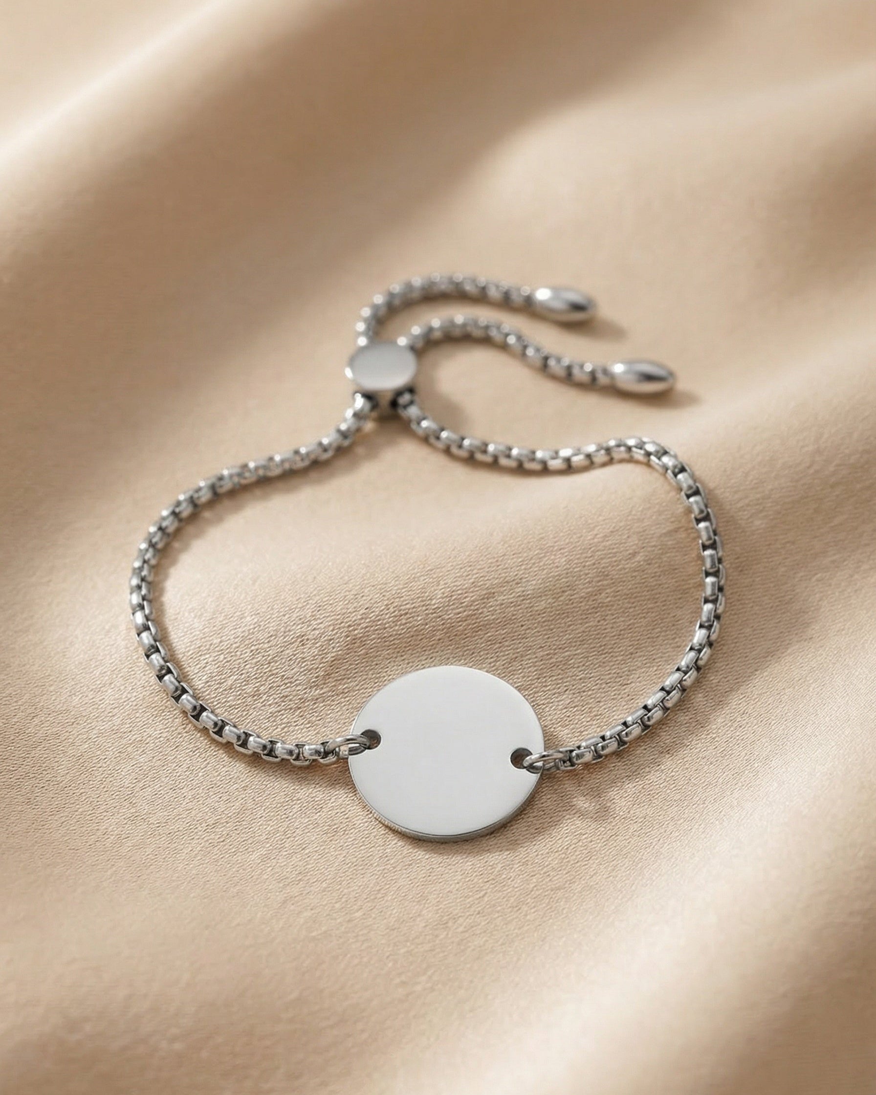 Silver bracelet with a round disc charm on a beige fabric background